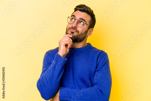 Valokuvatapetti Young caucasian man isolated on yellow background thinking and looking up, being reflective, contemplating, having a fantasy