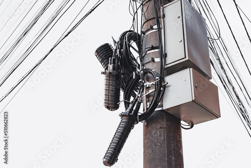 Fotografi Fiber optics connected to a black splice next to metallic boxes on a concrete pi