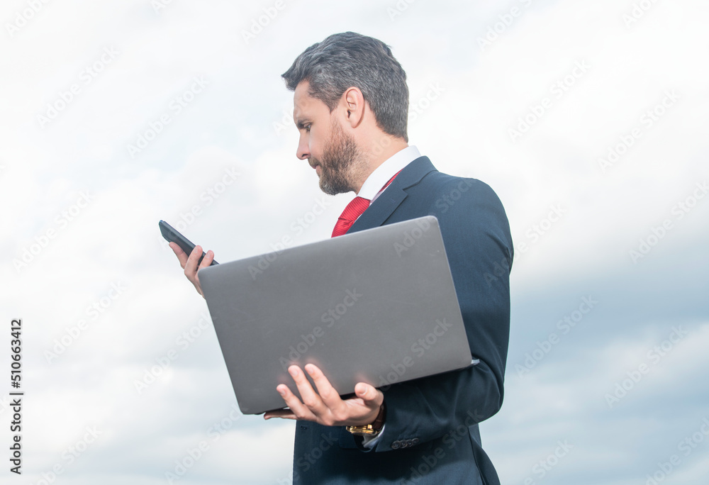 businessman in suit checking email on phone and hold laptop