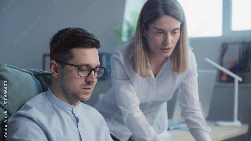 Smiling young man and woman talking using a computer working together in a modern office. On background businesspeople. Slow-motion Smiling young man and woman talking using a computer working together in a modern office. On background businesspeople. Slow-motion