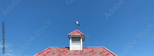 Toit en bois rouge avec une tour de clocher et une girouette pour indiquer l'orientation du vent. Ciel bleu.