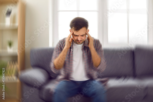 Man suddenly feels dizzy and takes a seat on the sofa. Young guy feeling pain and spinning sensation in his head. Headache, vertigo, health problem, brain tumor concept photo