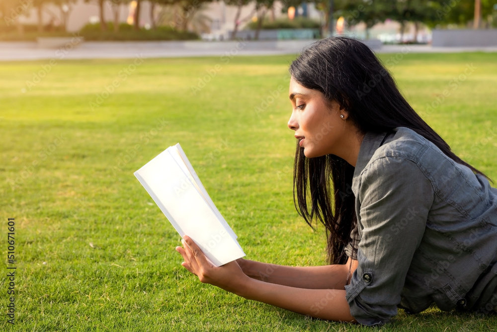 Close up portrait of young Indian ethnicity beautiful girl reading a book, laying on a grass Close up portrait of young Indian ethnicity beautiful girl reading a book, laying on a grass