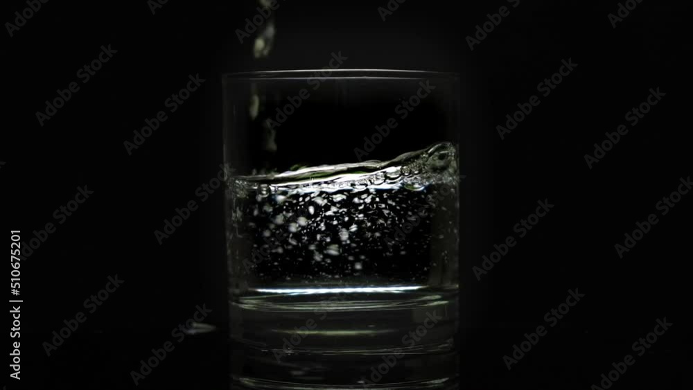 Ice water is poured into a smooth glass on a black background. Ice water is poured into a smooth glass on a black background.