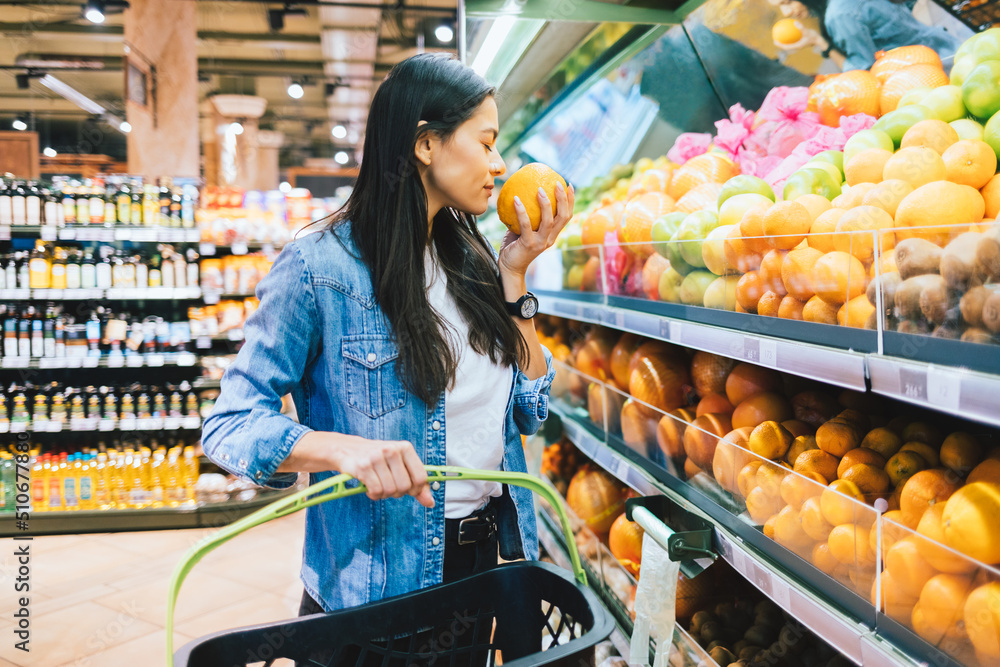 Young woman in supermarket near shelf with fruits chooses oranges