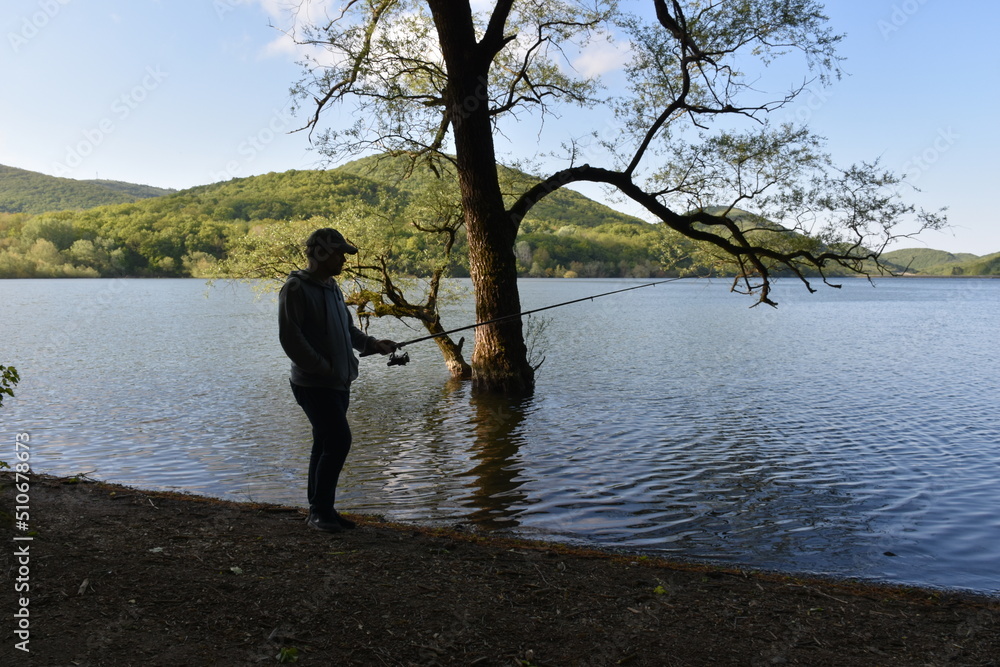 silhouette of a fisherman in a baseball cap on the shore of the lake