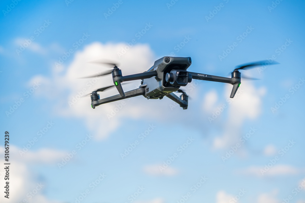 DJI Mavic 3 drone hanging in the air with fastspinning propellers on sky background Stock Photo