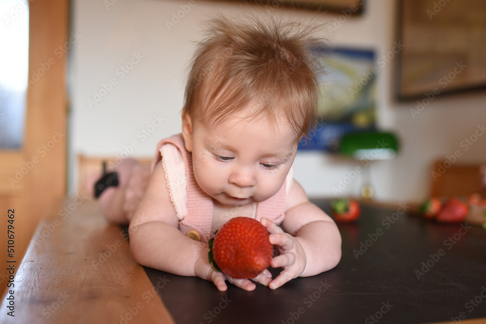 a little beautiful girl lies on the table with strawberries in her hands. baby in the kitchen. baby smiling a little beautiful girl lies on the table with strawberries in her hands. baby in the kitchen. baby smiling