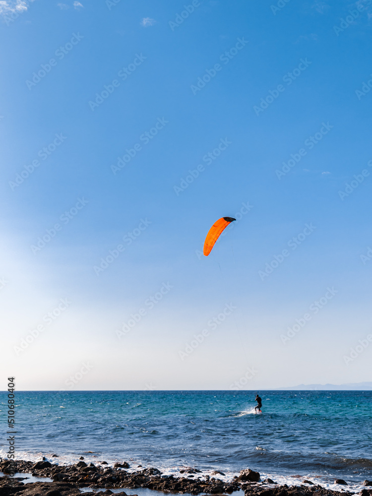 Person kiteboarding on sea waves on blue skyline background. Kitesurfing on Cyprus Person kiteboarding on sea waves on blue skyline background. Kitesurfing on Cyprus