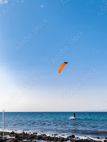 Person kiteboarding on sea waves on blue skyline background. Kitesurfing on Cyprus