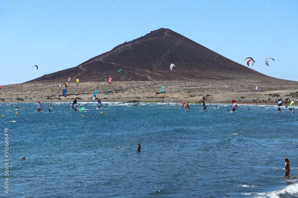 El Medano, Tenerife, Spain, March 8, 2022: Kitesurfers and bathers at the Red Mountain beach of el Medano with the Red Mountain in the background, Tenerife, Spain