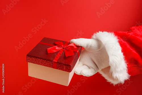 Santa Claus hand holding gift box on red background