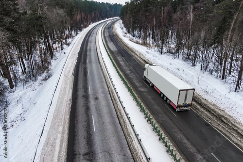 white truck on the higthway. cargo driving by road seen from the air. Top view landscape. shooting from a drone. Cargo delivery in winter. Aerial view of snow covered road in winter forest