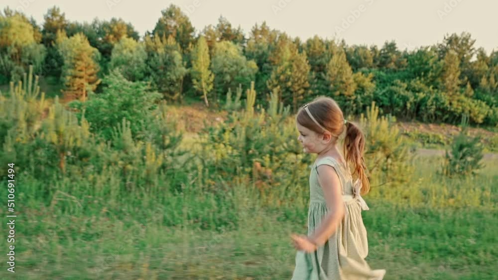 Cute little girl in a green summer dress with a smile runs across the lawn to meet dad, the father lifts the child in his arms and circles with her. Cute little girl in a green summer dress with a smile runs across the lawn to meet dad, the father lifts the child in his arms and circles with her.