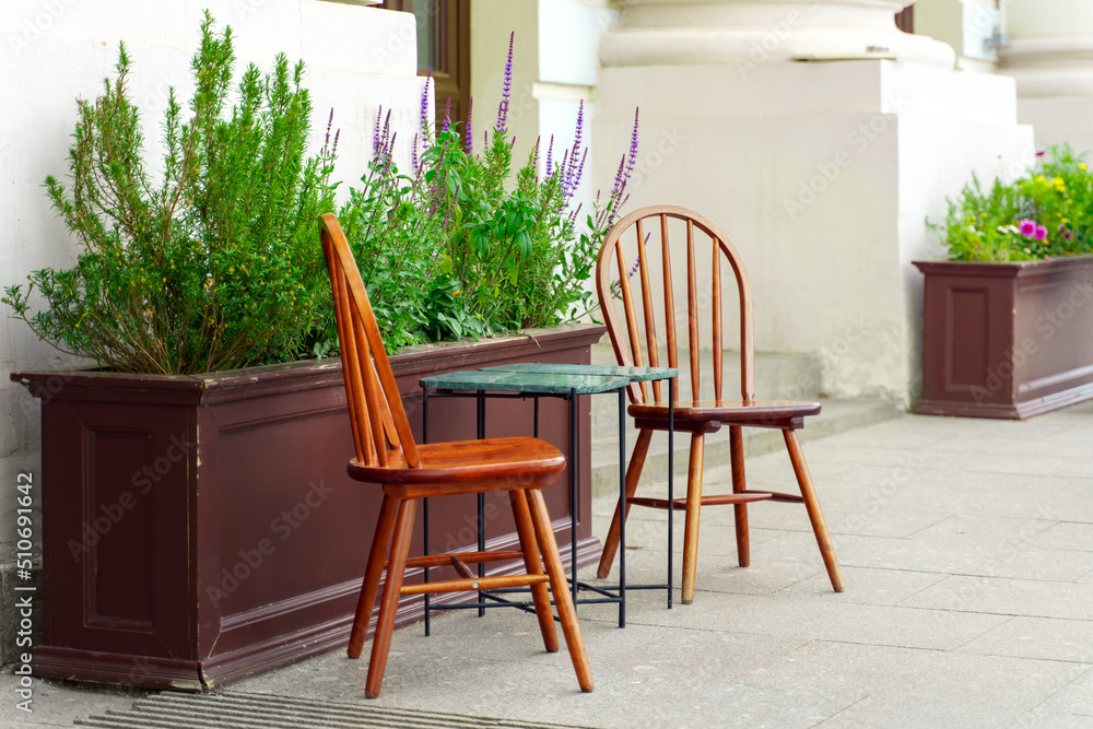 Elegant wooden chairs and a table with stone countertops stand on the sidewalk