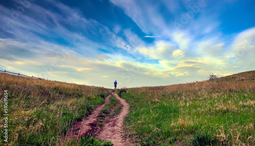Lone individual walks on a country path with dramatic clouds in the background