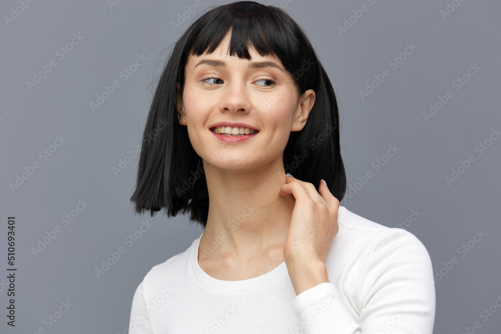 a relaxed woman stands against a dark background in a tight white T-shirt, calmly looks forward with her hand on her neck a relaxed woman stands against a dark background in a tight white T-shirt, calmly looks forward with her hand on her neck