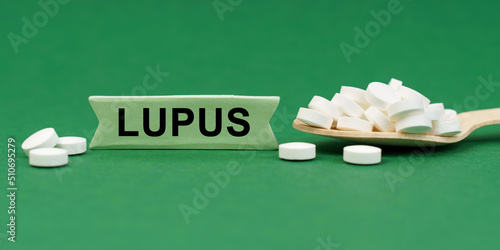 On a green surface, a wooden spoon with pills and a sign with the inscription - LUPUS photo
