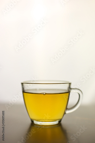 Brewed herbal green tea in a transparent cup on a dark table with a bright white light on the background