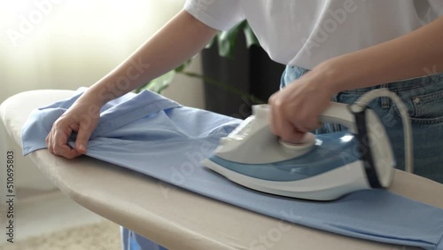 Young woman in white shirt ironing husband's blue shirt with iron. Home routine. housework and housekeeping concept. Faceless. 4k footage