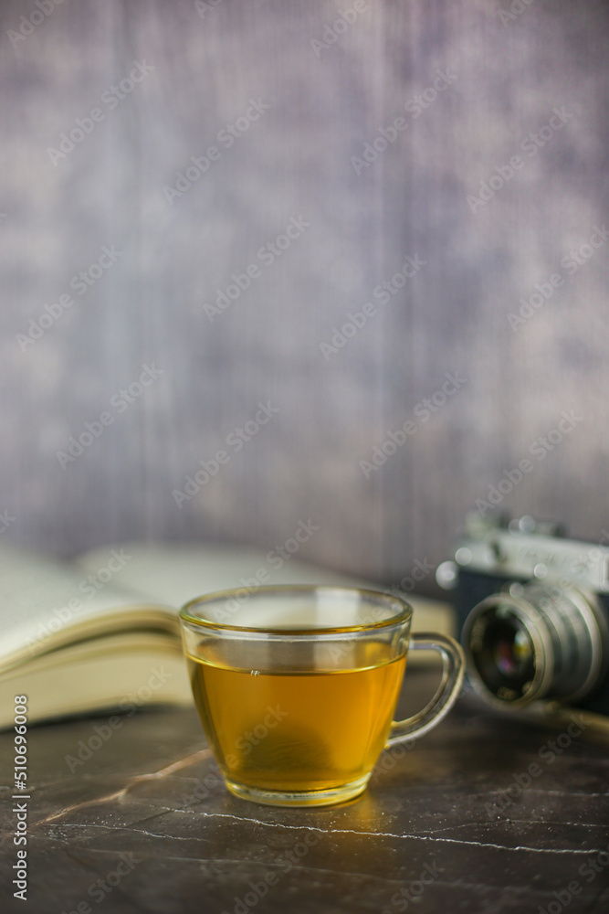 Brewed herbal green tea in transparent cup near open book and vintage camera on dark background Brewed herbal green tea in transparent cup near open book and vintage camera on dark background