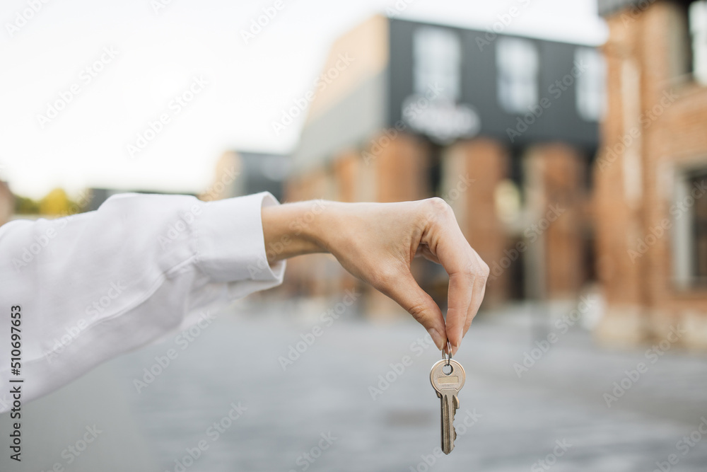 House keys in female hand on background of new buildings and sky. Real estate agent, moving home or renting property. Woman hand holds the keys to an apartment against the background of buildings. House keys in female hand on background of new buildings and sky. Real estate agent, moving home or renting property. Woman hand holds the keys to an apartment against the background of buildings.