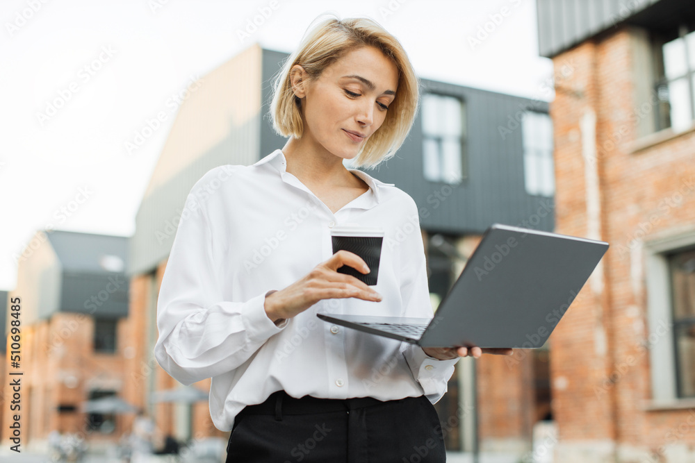 Portrait of cheerful caucasian woman having cup of take away fresh beverage talking to partner having online video chat using laptop walking on city street looking at screen. Portrait of cheerful caucasian woman having cup of take away fresh beverage talking to partner having online video chat using laptop walking on city street looking at screen.