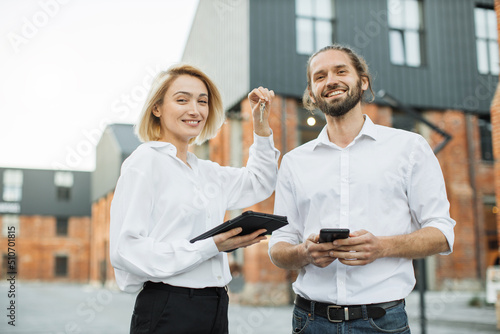 Happy man receiving keys from realtor woman at meeting, excited businessman purchasing real estate, making successful deal, attractive male buying first own dwelling, new apartment, mortgage or rent