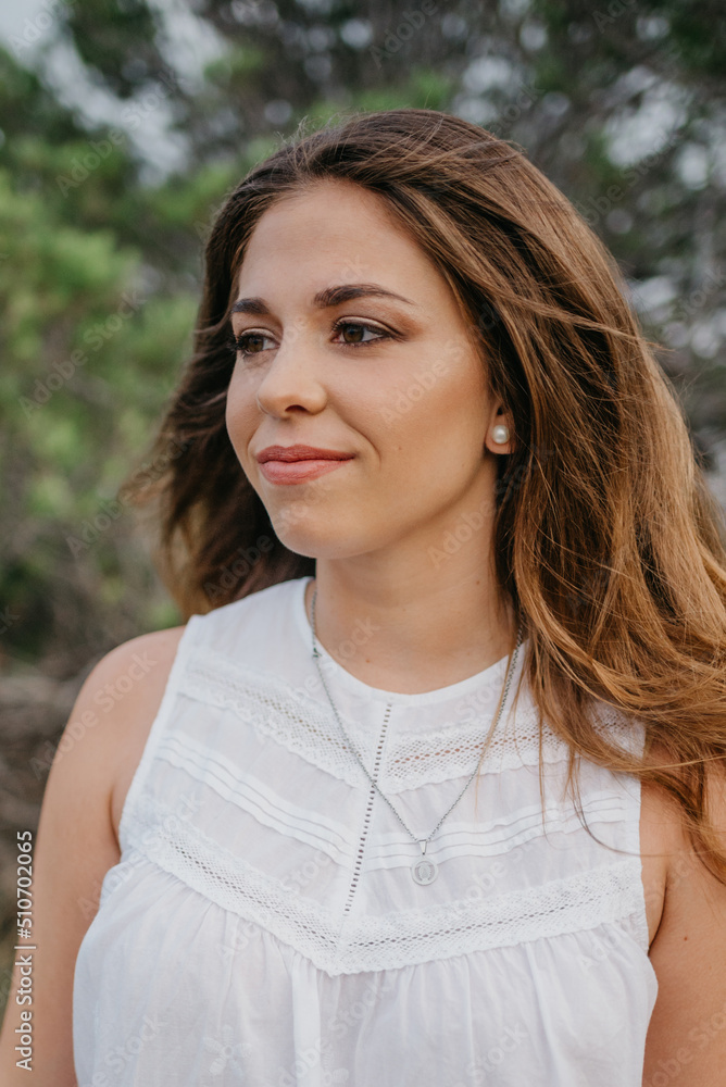 A close portrait of a Hispanic woman with green trees in the background in the highland park in Spain. A tourist is enjoying hiking at sunset in Valencia. A close portrait of a Hispanic woman with green trees in the background in the highland park in Spain. A tourist is enjoying hiking at sunset in Valencia.