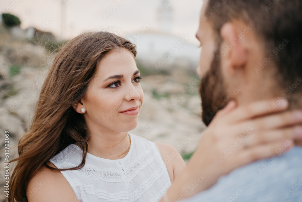 A close portrait of a Latin girl who is holding the neck of her Hispanic boyfriend near the lighthouse in Spain. A smiling couple of tourists in the evening in Valencia. A close portrait of a Latin girl who is holding the neck of her Hispanic boyfriend near the lighthouse in Spain. A smiling couple of tourists in the evening in Valencia.