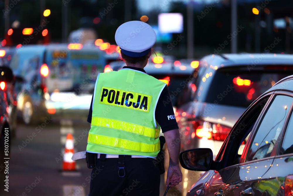 Policjantka kieruje ruchem drogowym wieczorem podczas szczytu w korkach ulicznych.  - obrazy, fototapety, plakaty 