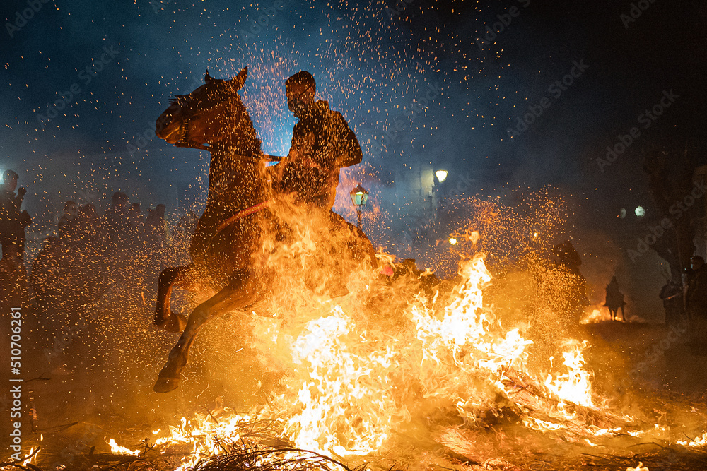 horses with their riders jumping bonfires as a tradition to purify animals.. - obrazy, fototapety, plakaty 