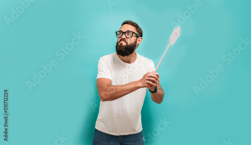 Young caucasian charismatic man holding a fly swatter wanting to kill annoying mosquito or a fly. photo