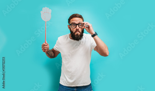 Fotografie Young caucasian charismatic man holding a fly swatter wanting to kill annoying mosquito or a fly