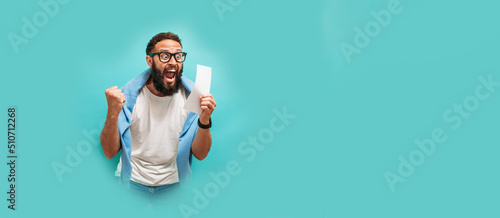 Fotografia Excited happy young male winner feeling joy winning lottery, placing bets, getting cashback online gift isolated on blue background