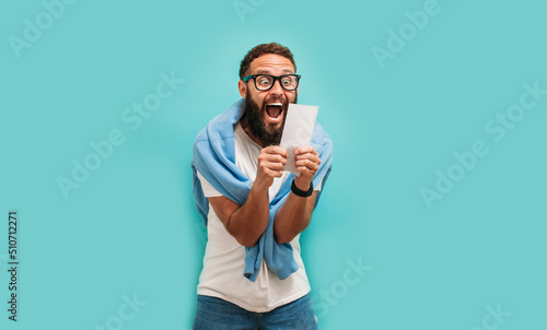 Fotografia Excited happy young male winner feeling joy winning lottery, placing bets, getting cashback online gift isolated on blue background