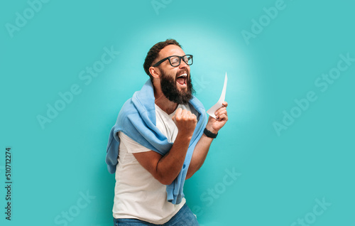 Excited happy young male winner feeling joy winning lottery, placing bets, getting cashback online gift isolated on blue background. Human face emotions and betting concept. Trendy colors photo