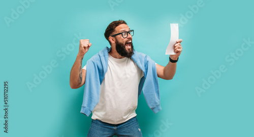 Fotografie, Obraz Excited happy young male winner feeling joy winning lottery, placing bets, getting cashback online gift isolated on blue background