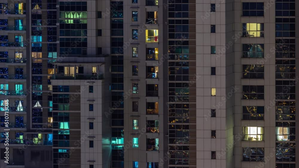 Apartment windows of a glazed skyscraper glow at night with city lights reflection aerial timelapse. Illuminated towers with balconies Apartment windows of a glazed skyscraper glow at night with city lights reflection aerial timelapse. Illuminated towers with balconies