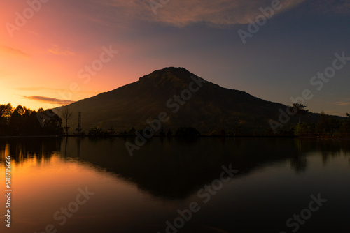 Sunrise with Mount Sumbing with lake surface on the foreground. The lake surface make reflection of mountain and sunrise sky. Embung Kledung  Central Java  Indonesia 