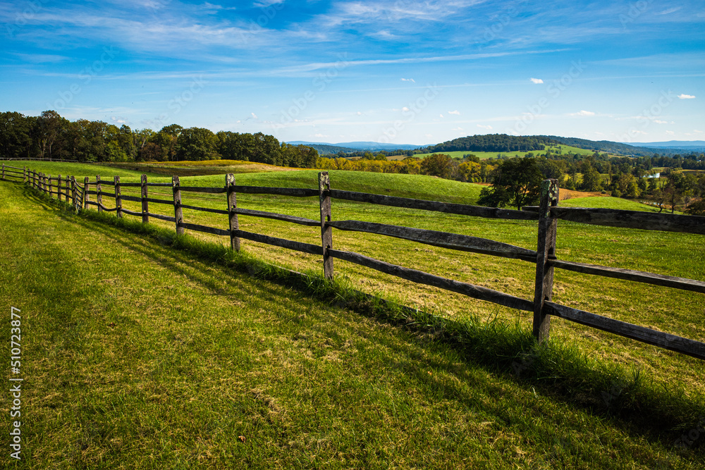 Meadow with wooden fence, green grass, hilly landscape and blue sky with white clouds on a beautiful summer day in the Sky Meadows State Park, Virginia, USA.