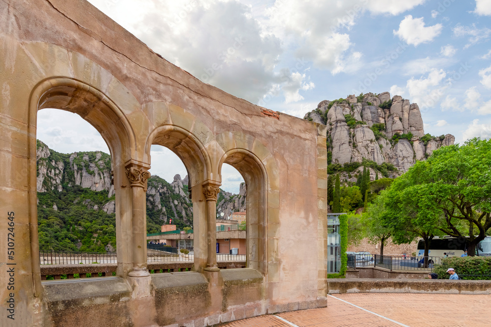 An ancient wall with arches with the Montserrat mountains and Santa Maria de Montserrat Abbey in view.