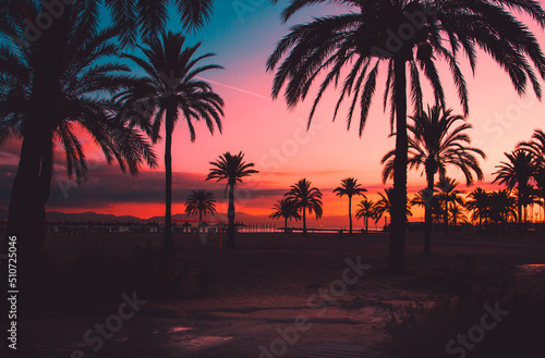 Fiery sunset on the coast. Relax atmosphere. Background sunset with silhouette palm trees, El Arenal, Mallorca. Bright saturated sunset on the sea and a rocking boat on the waves, Mallorca, Spain.