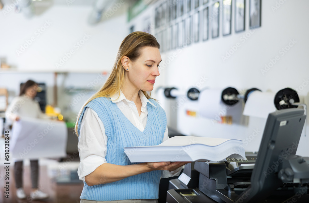 Woman loading ream of paper into printer while working in printing office.
