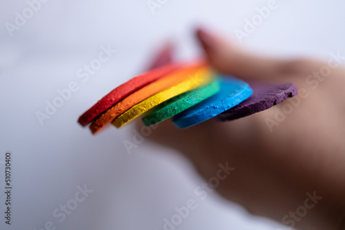 mano sosteniendo batelenguas de madera multicolor, con bandera de orgullo gay, sobre fondo blanco, pintado con pintura acrílica photo