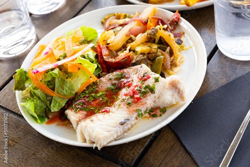 Traditional French fish dish of baked blue ling fillet with savory sauce, fresh green salad and vegetable saute.. photo