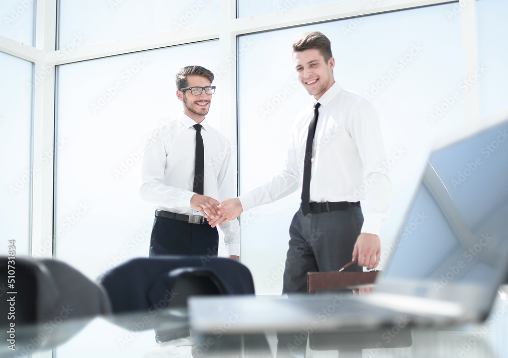 Two businessmen shaking hands standing at big window