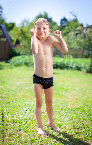 the boy stands on the grass in his swimming trunks and shivers from the cold on a sunny day, summer, rest