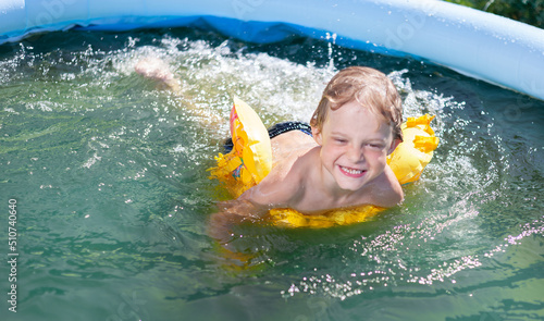 a child swims in an inflatable pool in the summer at the dacha, in a rubber inflatable circle, splashes and smiles and laughs