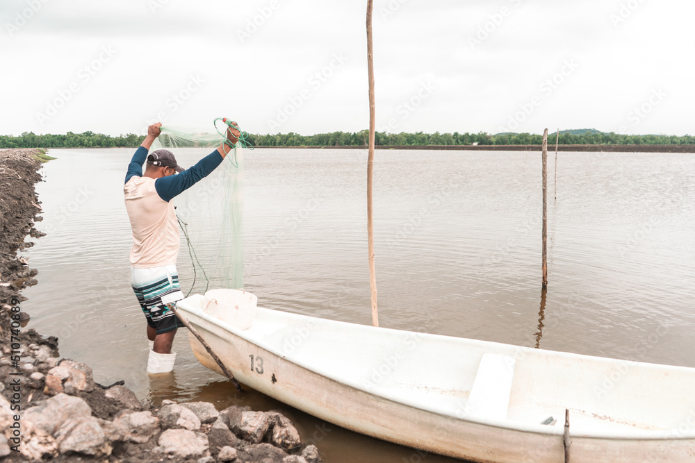 Latin American fisherman checking his net to catch farmed shrimp in his boat in a pond in Chinandega Nicaragua